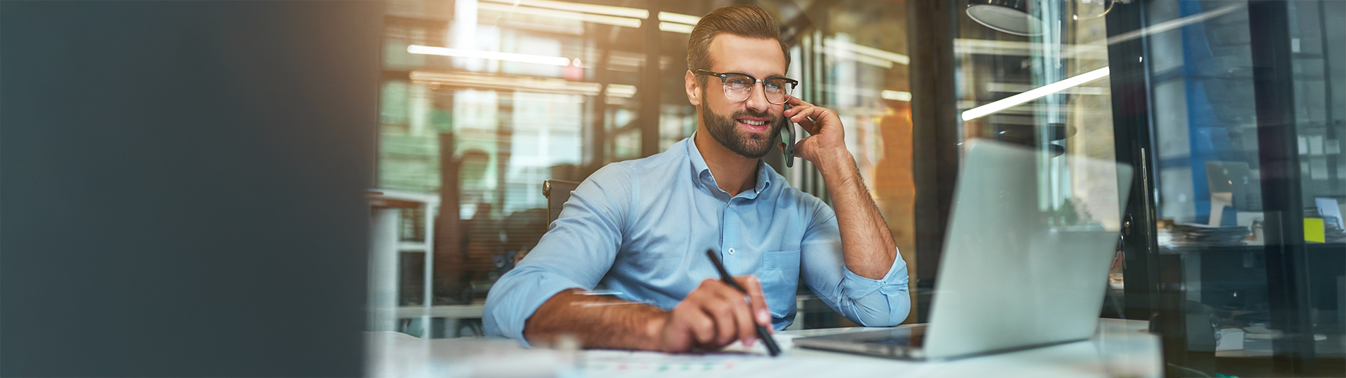 Profissional sorri satisfeito e confiante enquanto conversa ao celular e analisa dados financeiros em relatórios e no notebook, simbolizando o sucesso e a concretização da estratégia para recuperar o investimento da empresa.