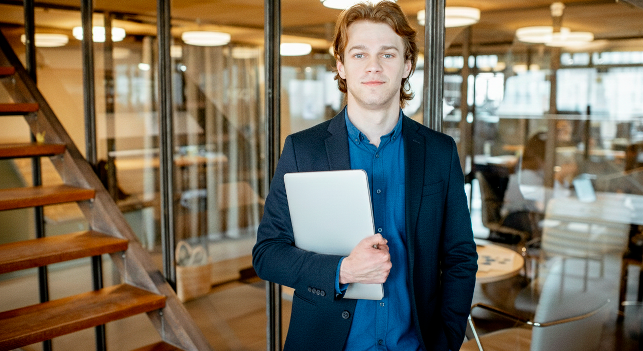 Foto em close de uma pessoa segurando um smartphone moderno em frente a um notebook. A imagem ilustra o conceito de Enterprise Mobility Management, focando na integração entre dispositivos móveis e o ambiente de trabalho digital.